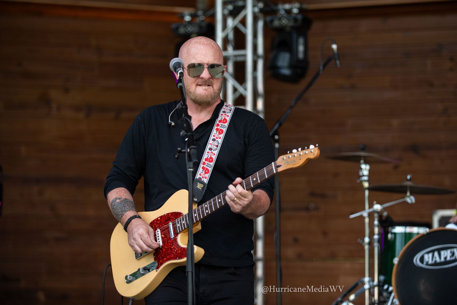 Musician performing on stage with a sunburst Telecaster guitar and wearing dark clothing at an outdoor venue.