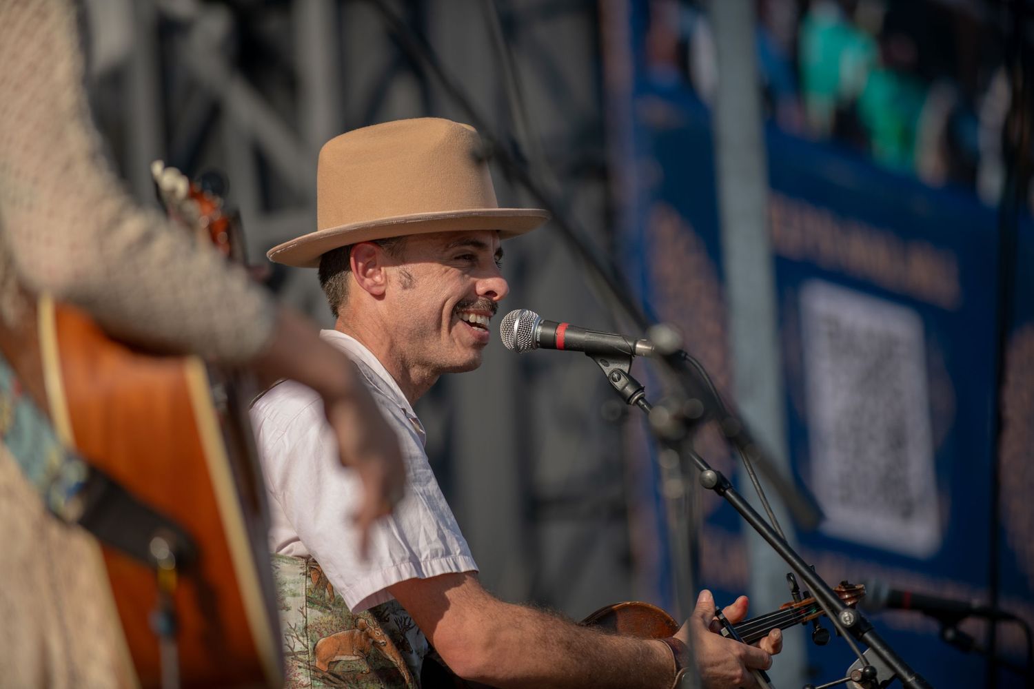 A country music performer in a cowboy hat sings into a microphone on stage during a live performance.