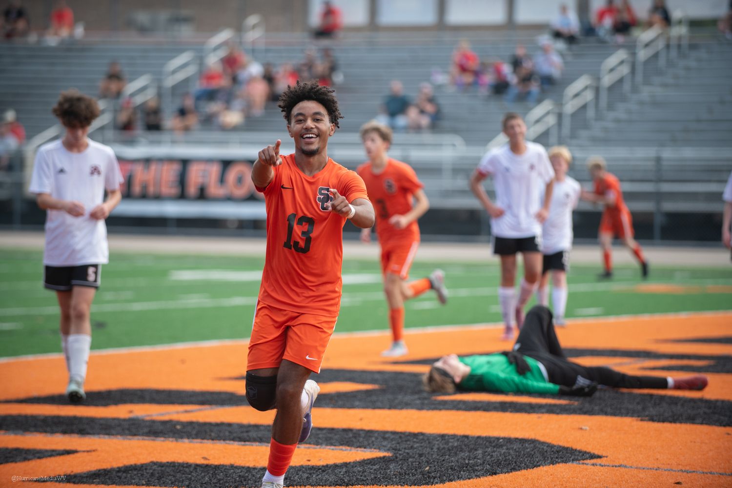 Soccer players compete on a field with orange and black turf during an intense match.