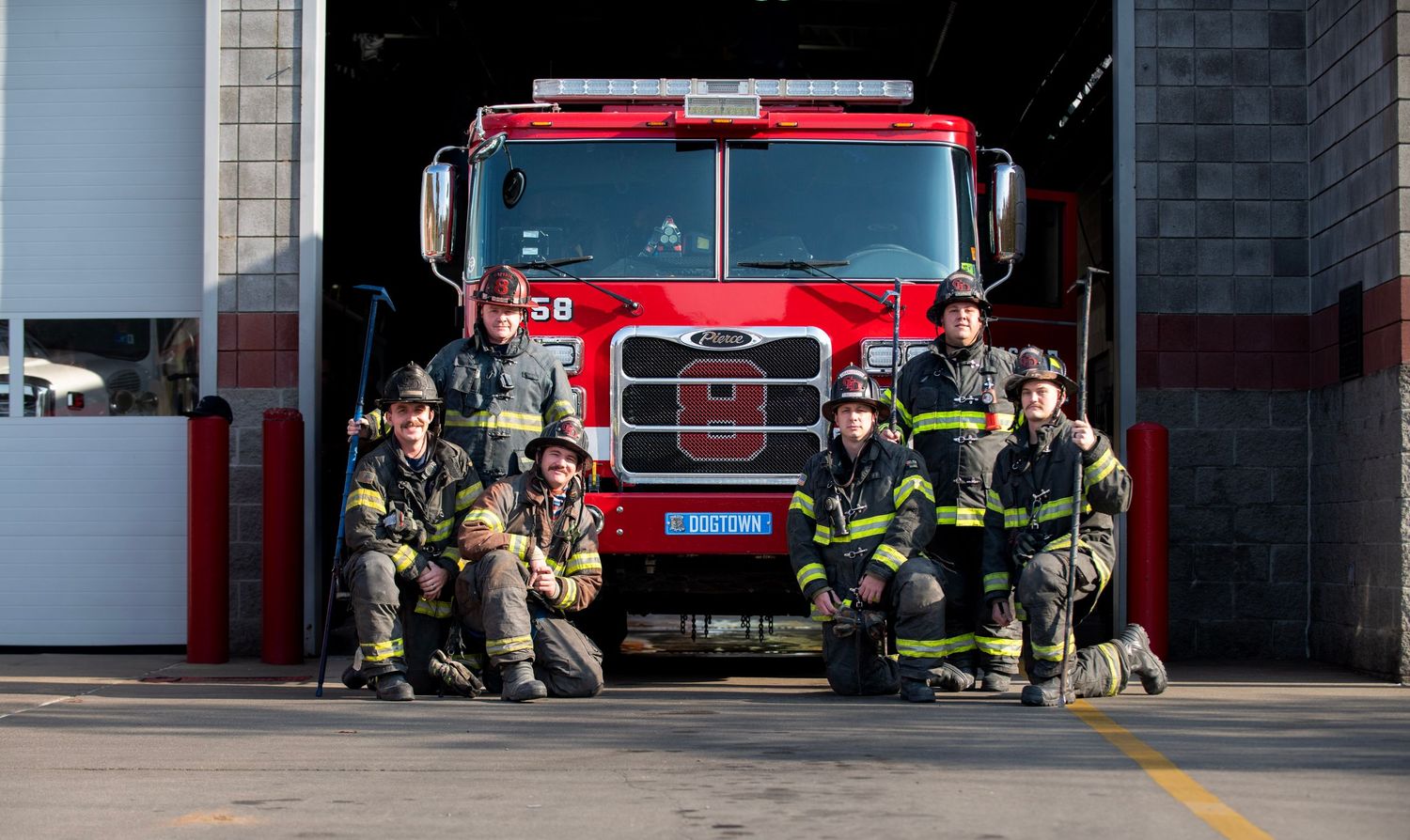 Fire truck crew poses in front of their red engine at the station bay.