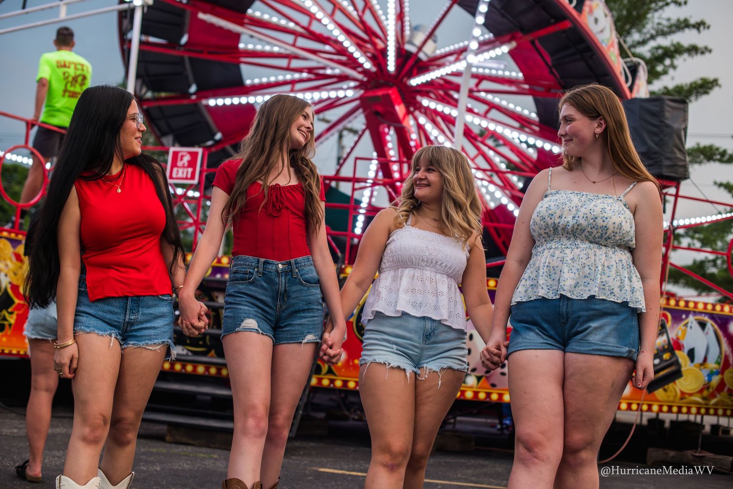 Group walks together at a carnival with a colorful ferris wheel in the background.
