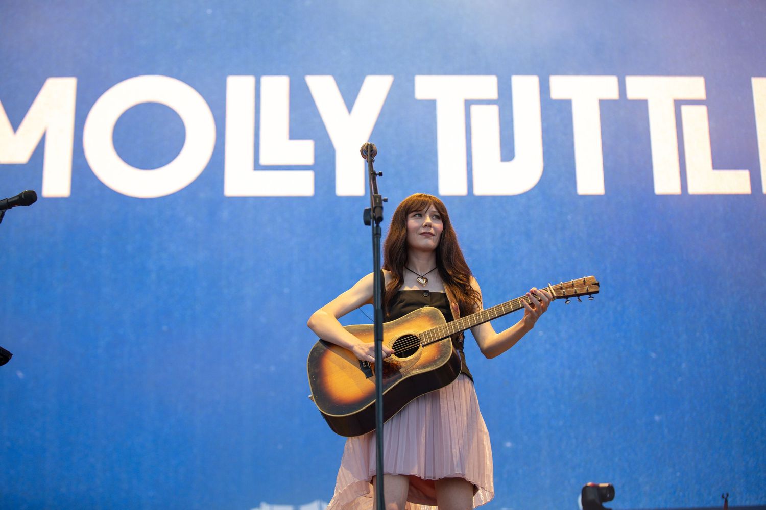 Musicians perform on stage with acoustic guitars against a vibrant blue backdrop during a live concert performance.
