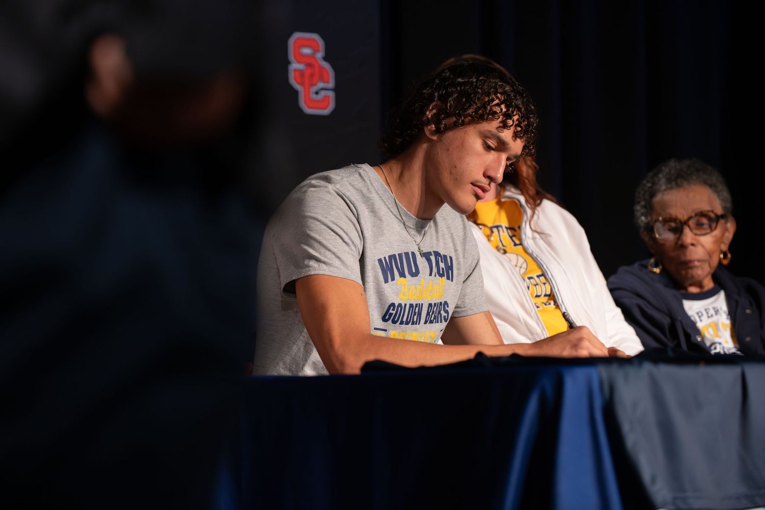 A student athlete signing papers at a table during a ceremony.
