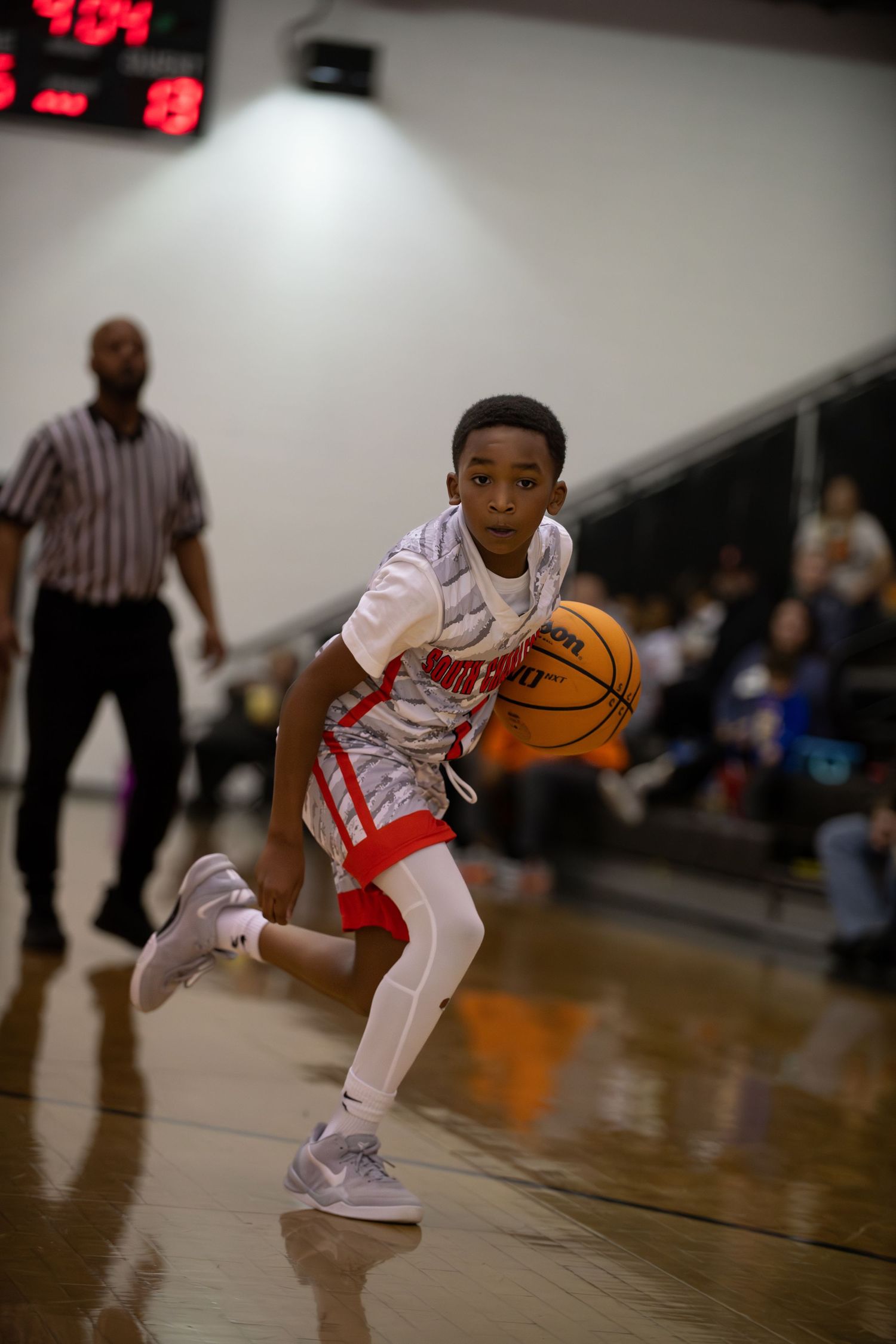 Young basketball player in white and red uniform dribbles while moving across court during game.