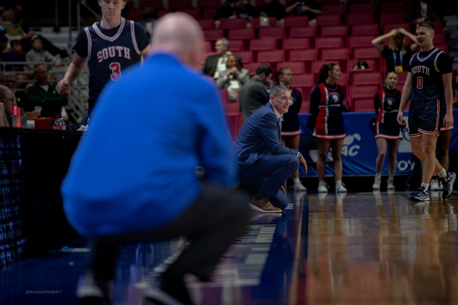 Coaches crouch on sideline during basketball game.