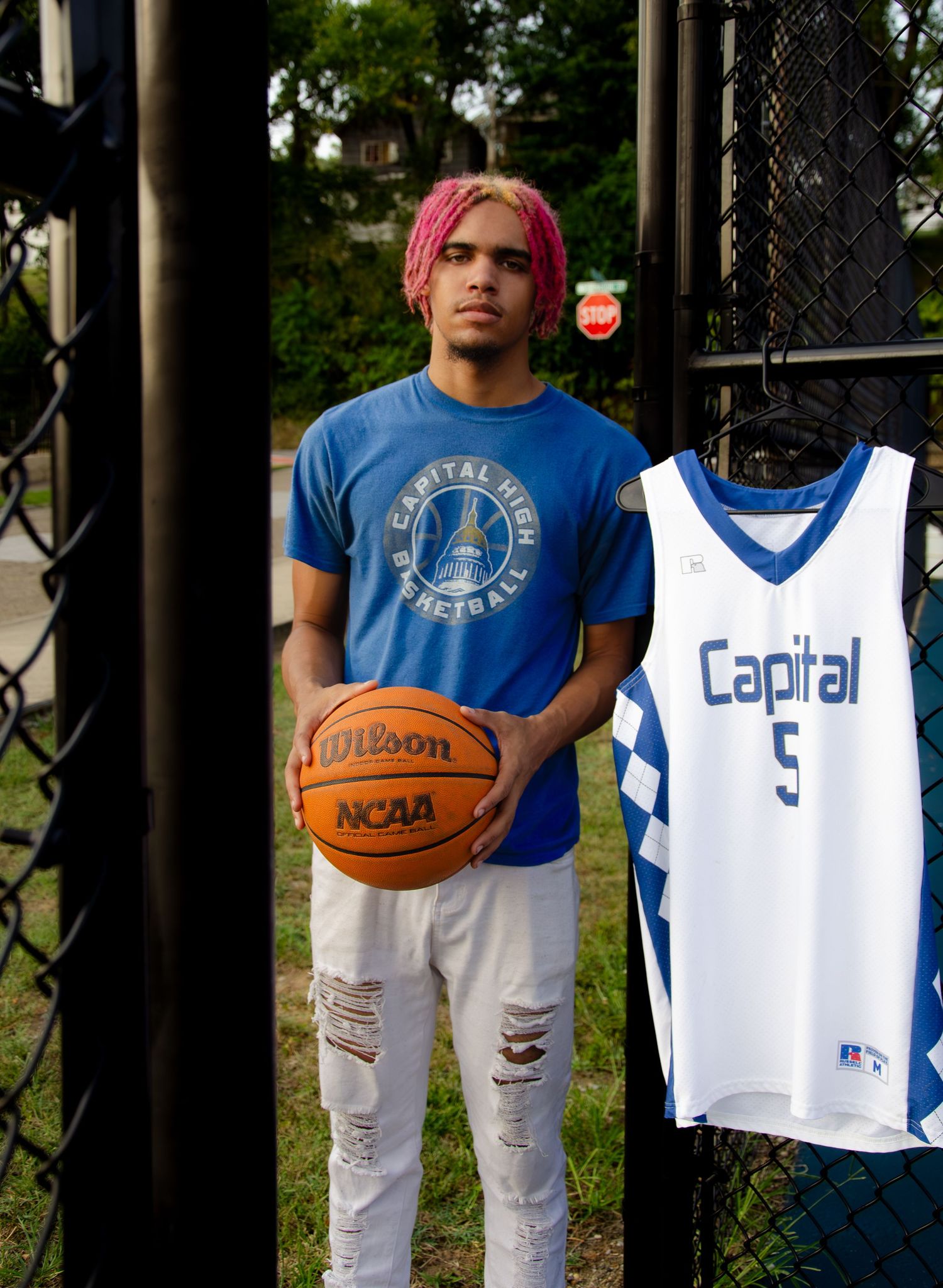 Basketball equipment and jerseys displayed against a chain link fence.