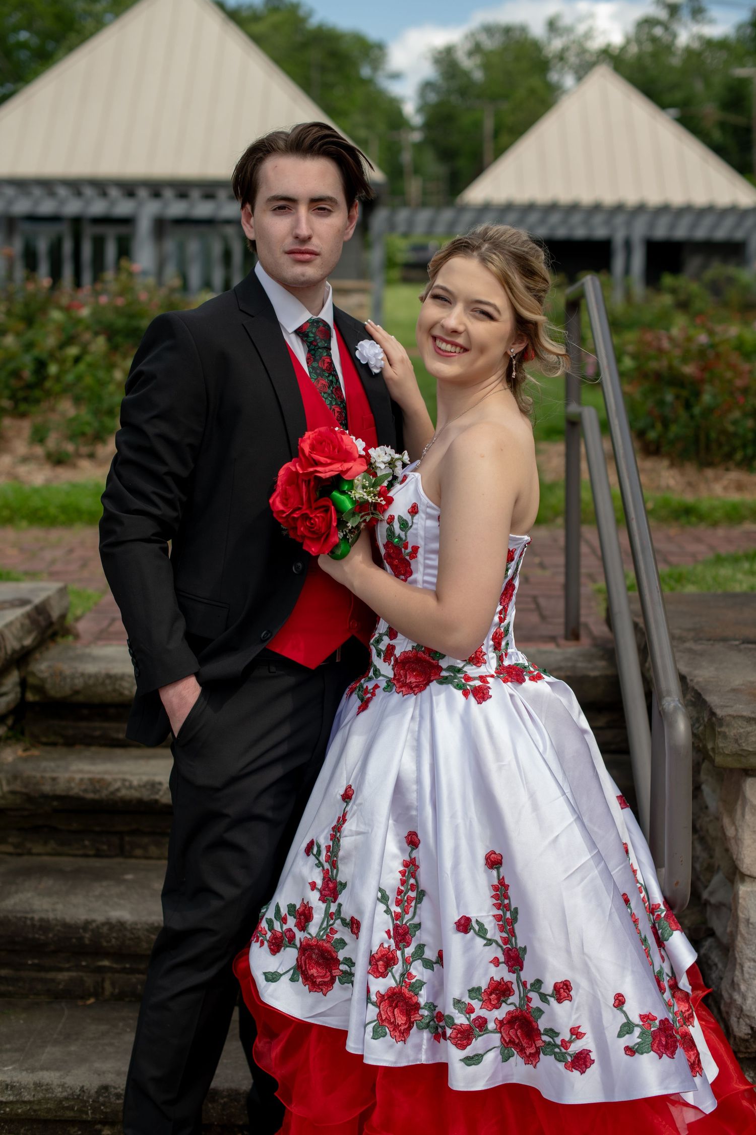 Couple in formal attire posing on stone steps with a stunning red and white floral dress.