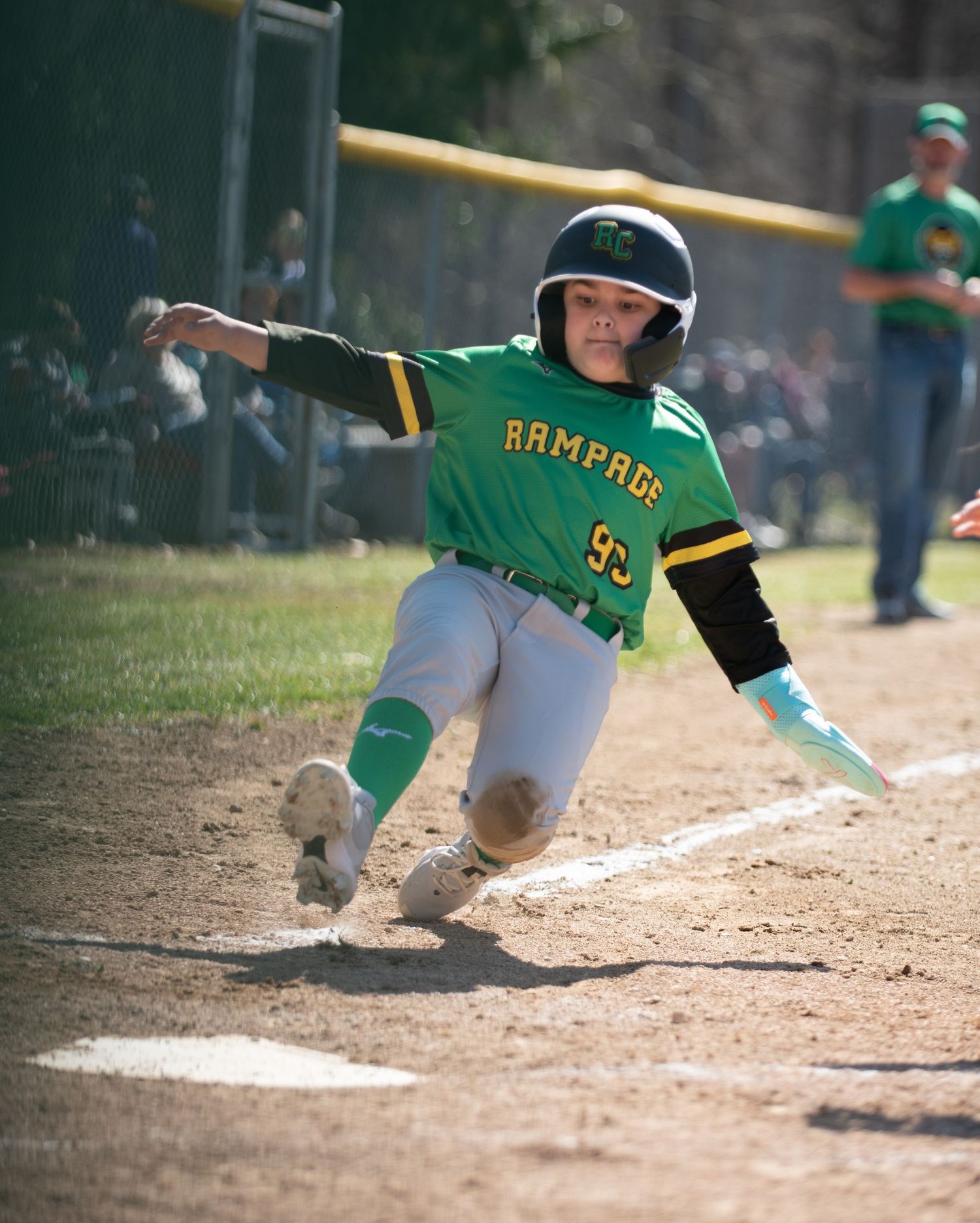 Baseball player in green Rampage uniform slides dramatically into home plate during game.