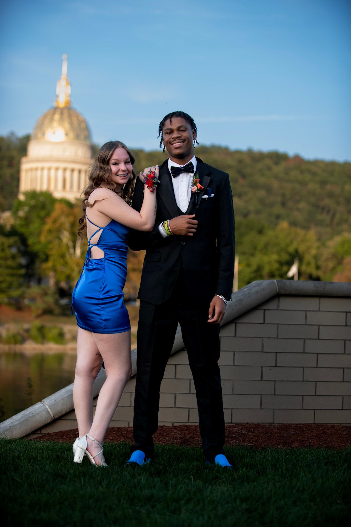 Couple in formal attire poses on brick wall with domed building visible in background.