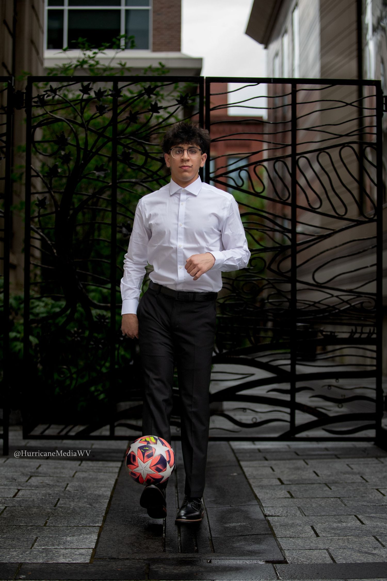 Person in formal white shirt and black pants posing with soccer ball near urban railing.