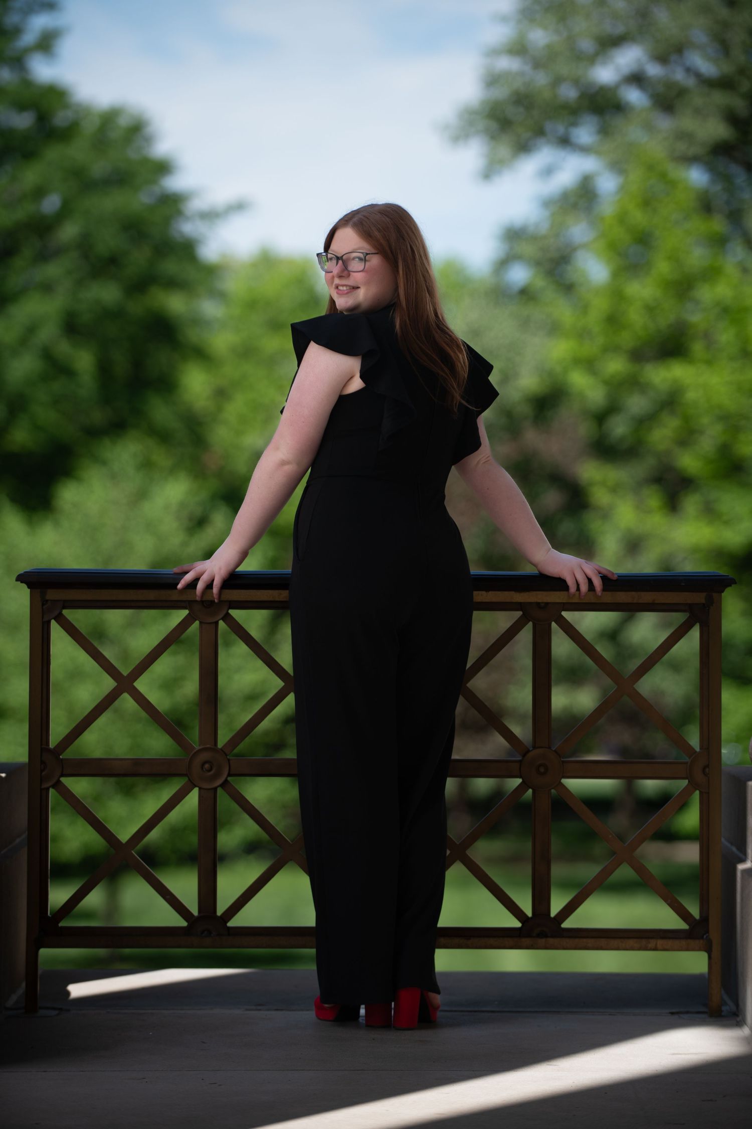 A figure in a black formal dress poses on a wooden deck railing.
