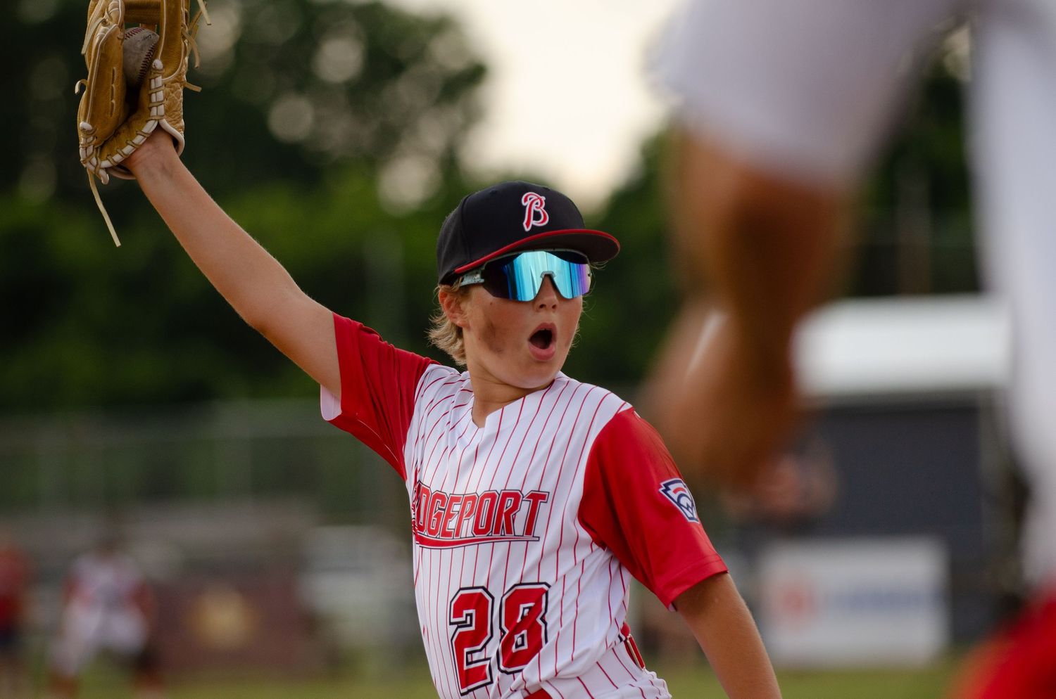 Baseball player in red and white uniform raises glove during game at sunset.