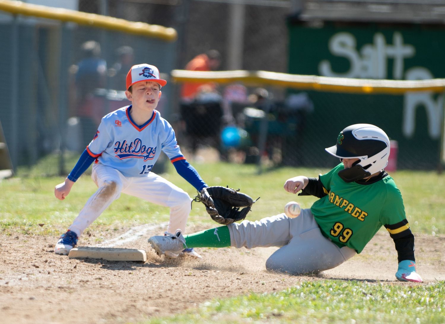 Baseball players engage in close play at base during youth league game.
