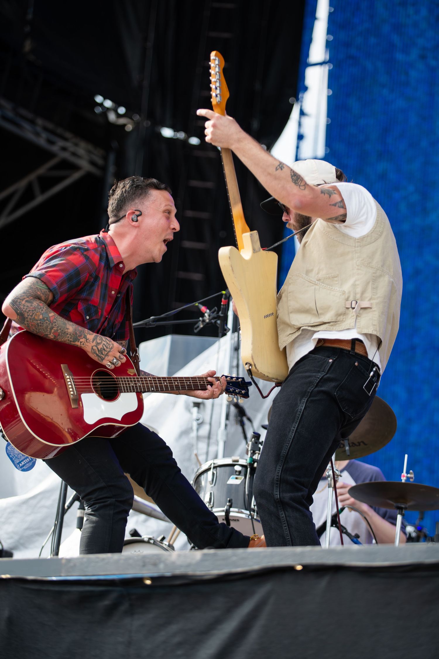 Musicians perform energetically on stage with acoustic guitars during an outdoor concert performance.