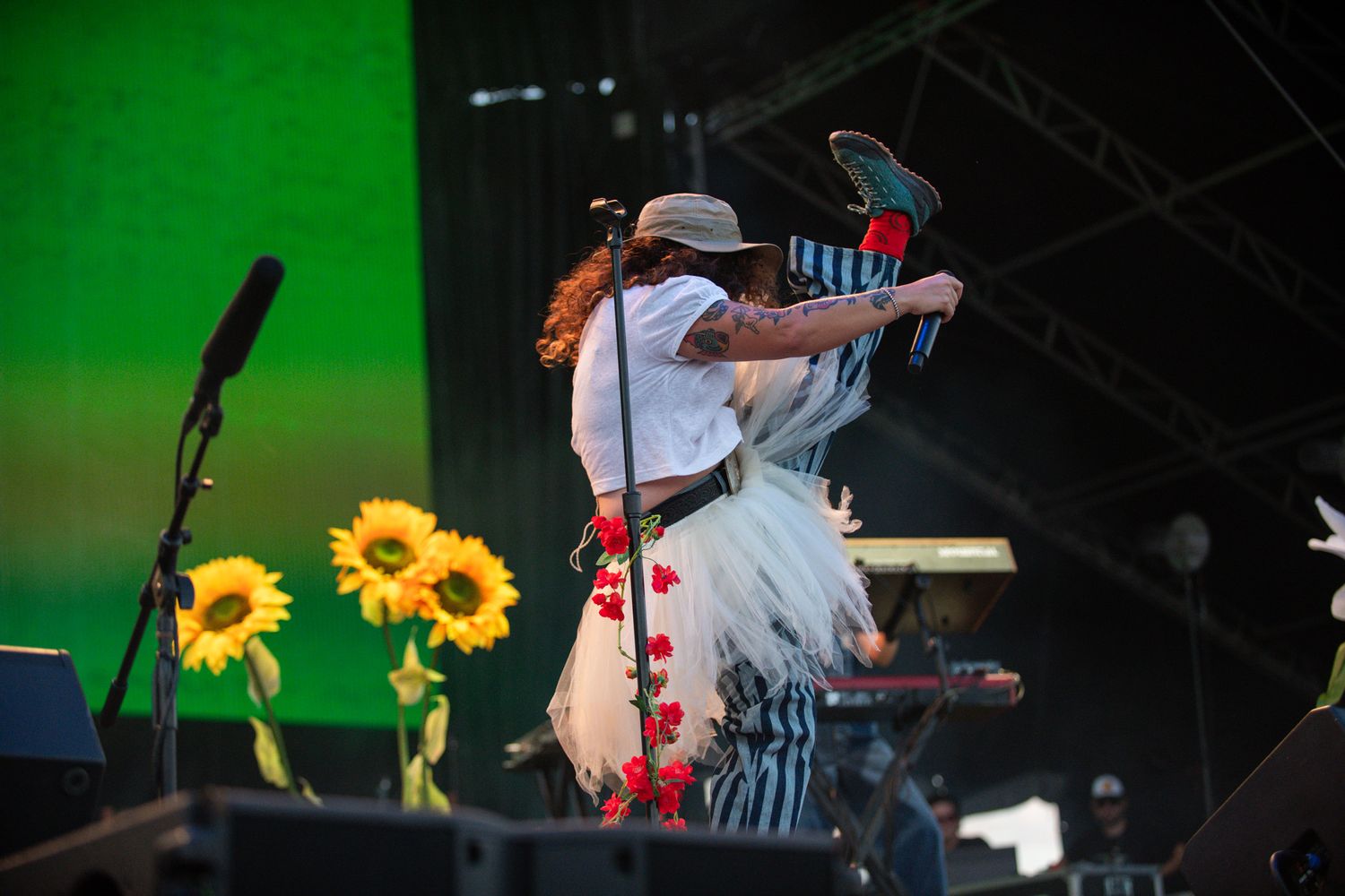 Musicians perform on stage with sunflowers and green lighting creating a vibrant concert atmosphere.