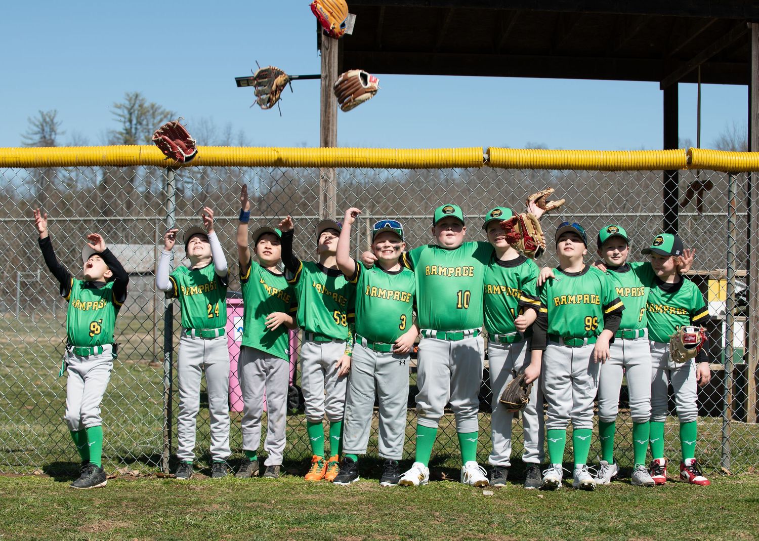 Youth baseball team in green uniforms celebrates together under a dugout roof.