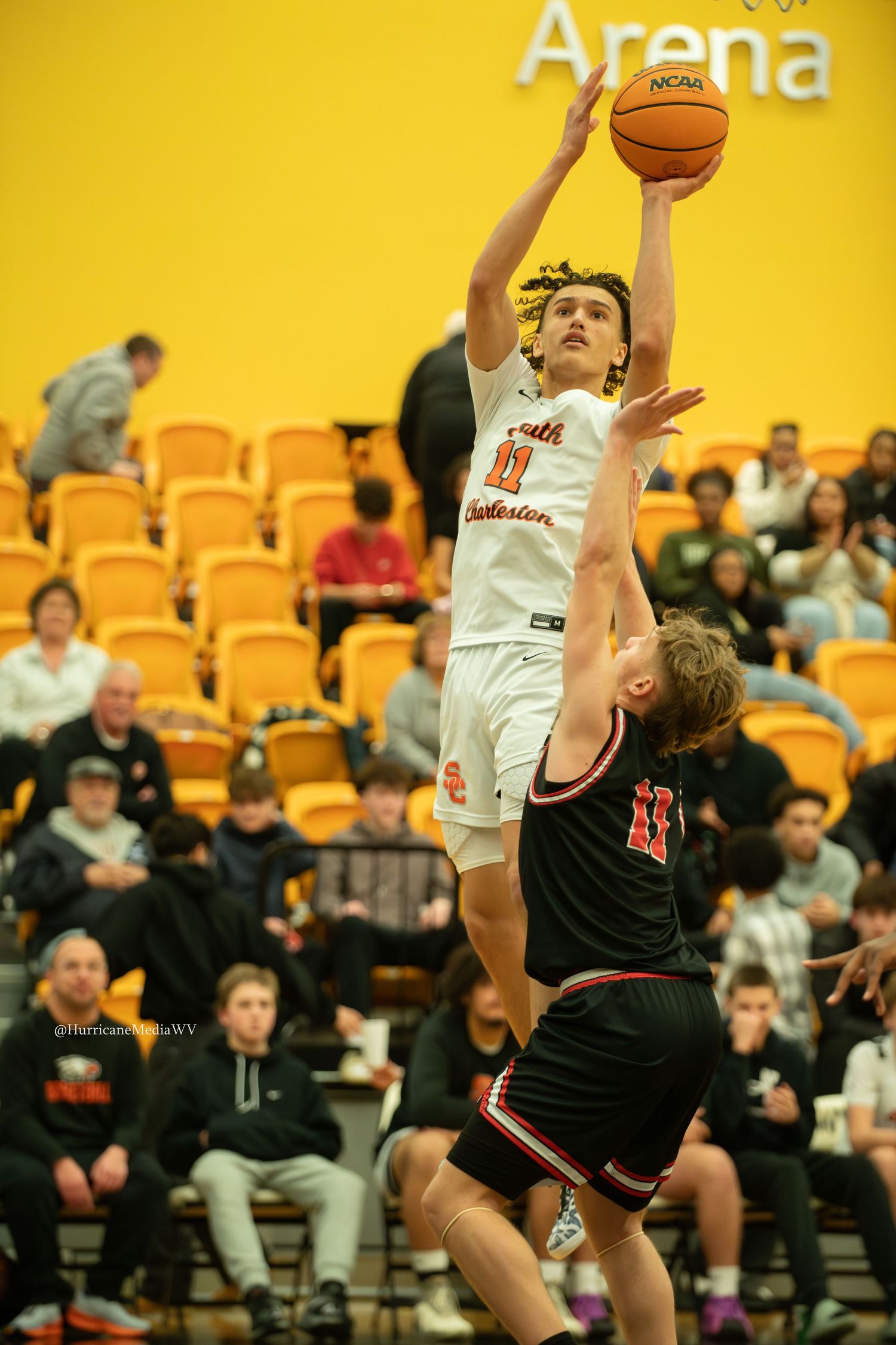 Basketball player in white jersey leaps for layup against defender in black uniform.