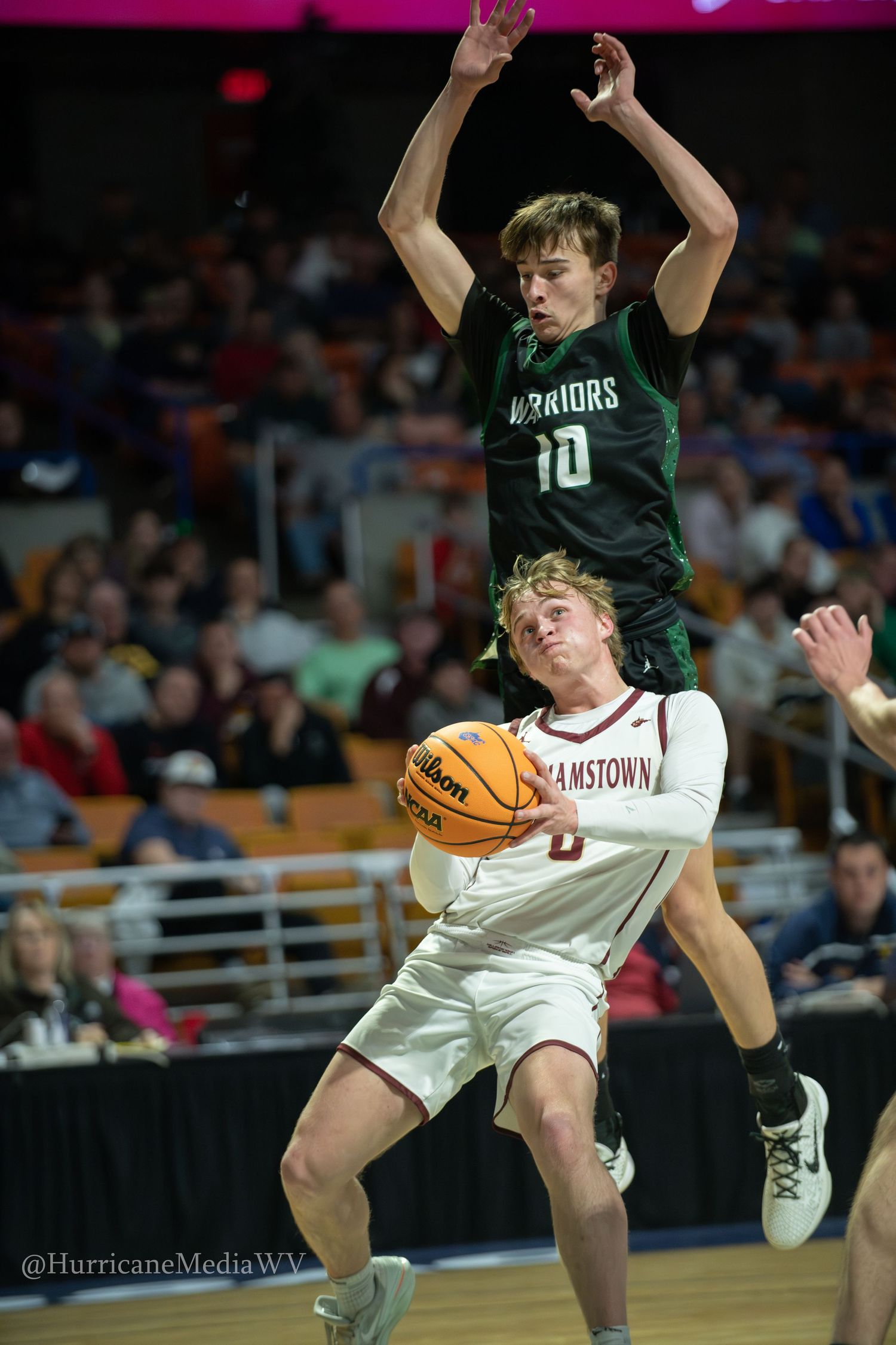 Basketball player in white uniform dribbles while defended by player in dark green jersey during competitive game.