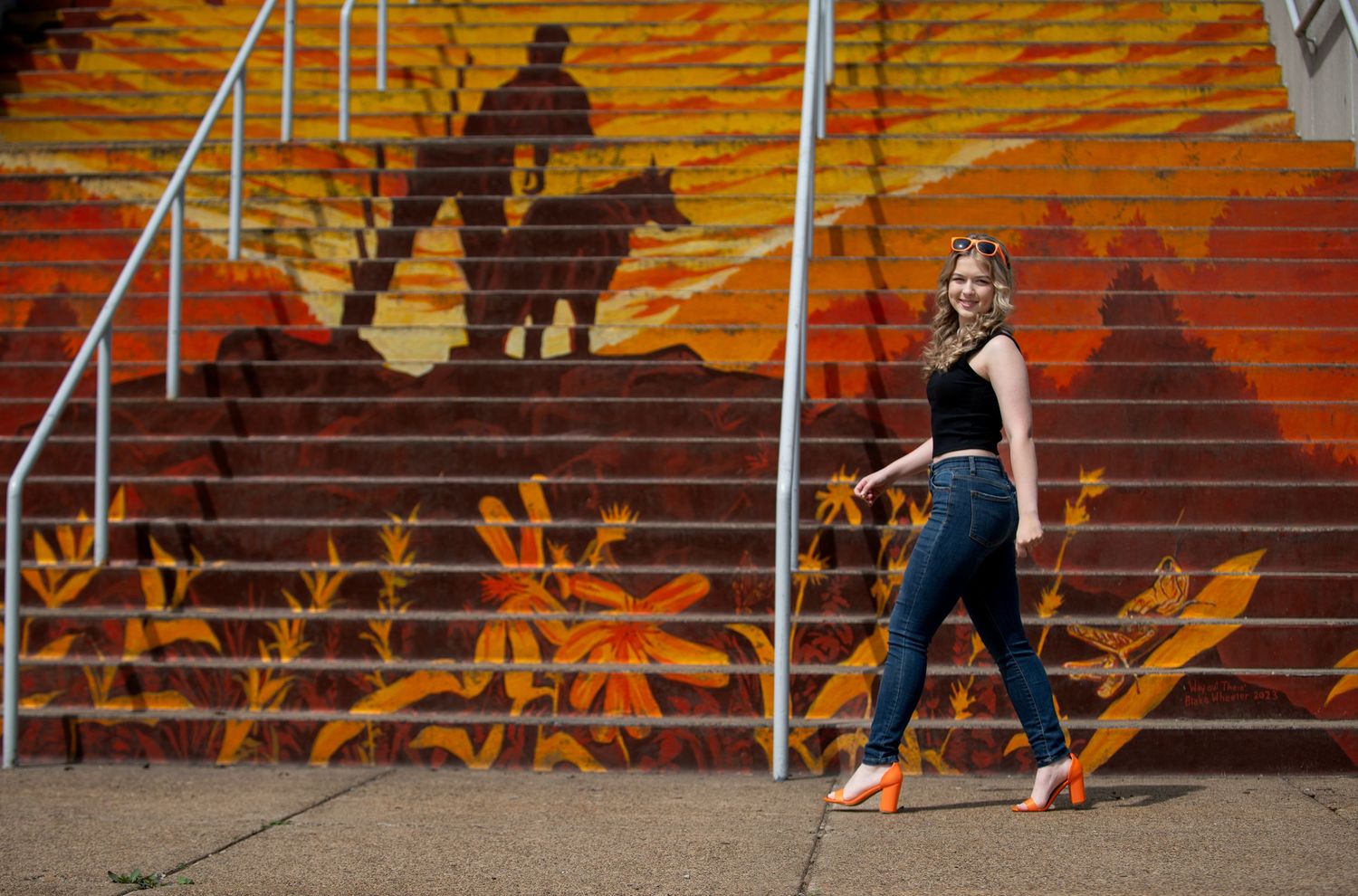 A person poses against vibrant orange street art on outdoor stairs.