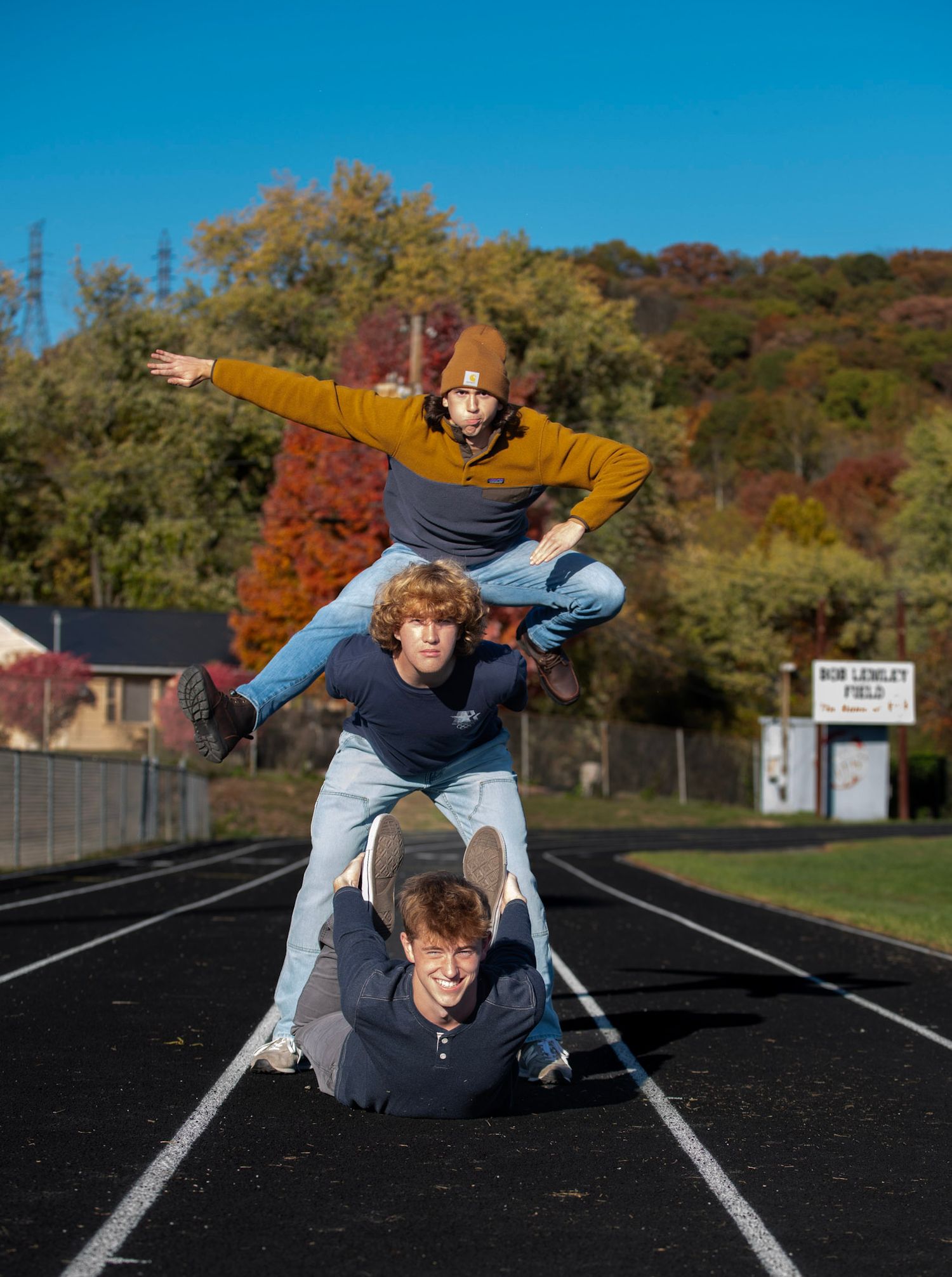 Three people stacked on top of each other create a playful pose on a track field.