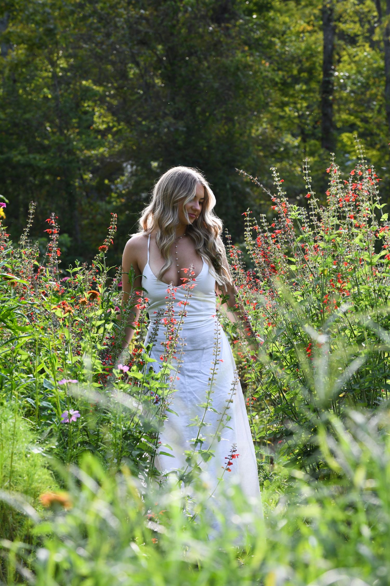 A white dress contrasts with vibrant wildflowers in a natural garden setting.