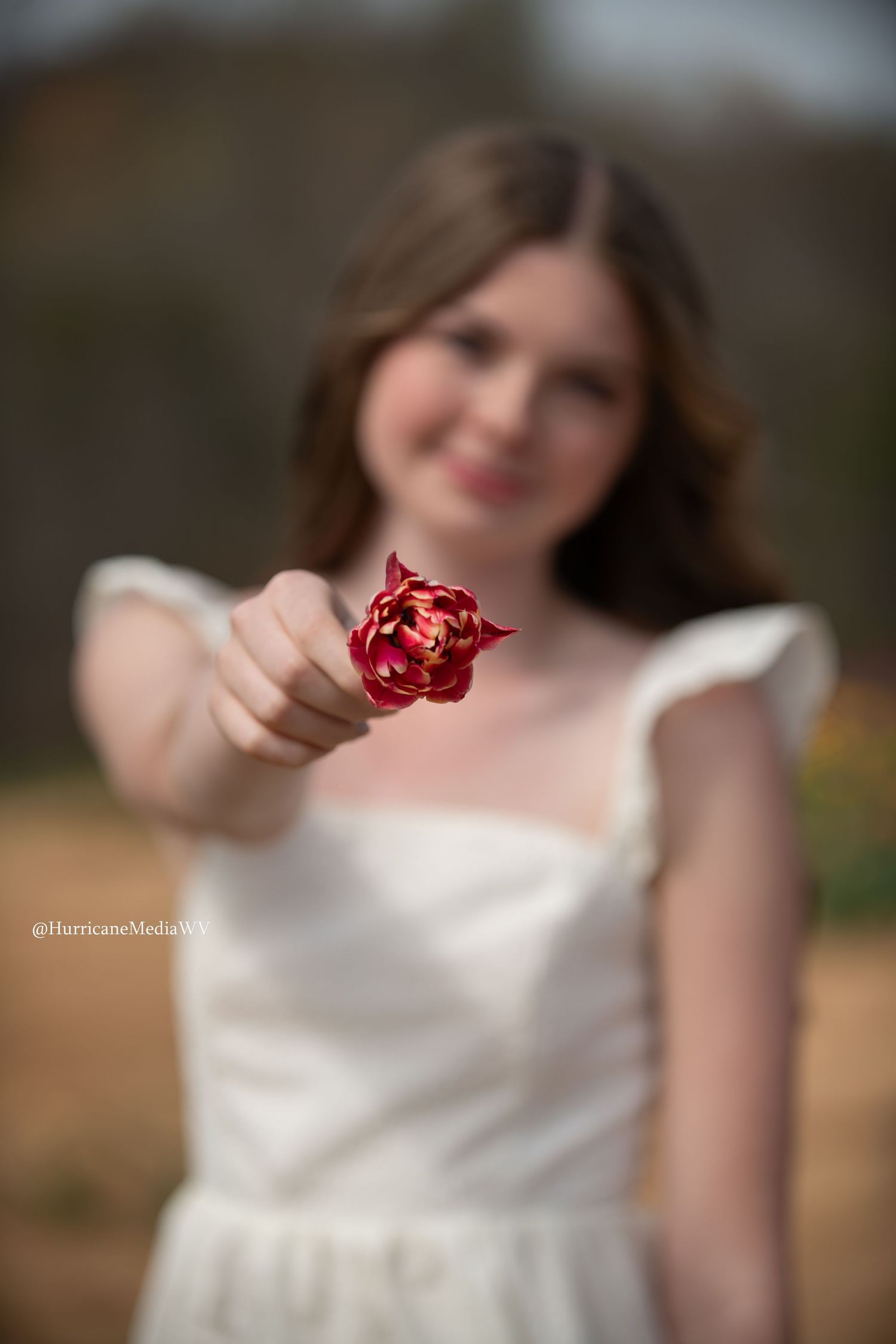 White-dressed figure holding a red decorative object against blurred background.