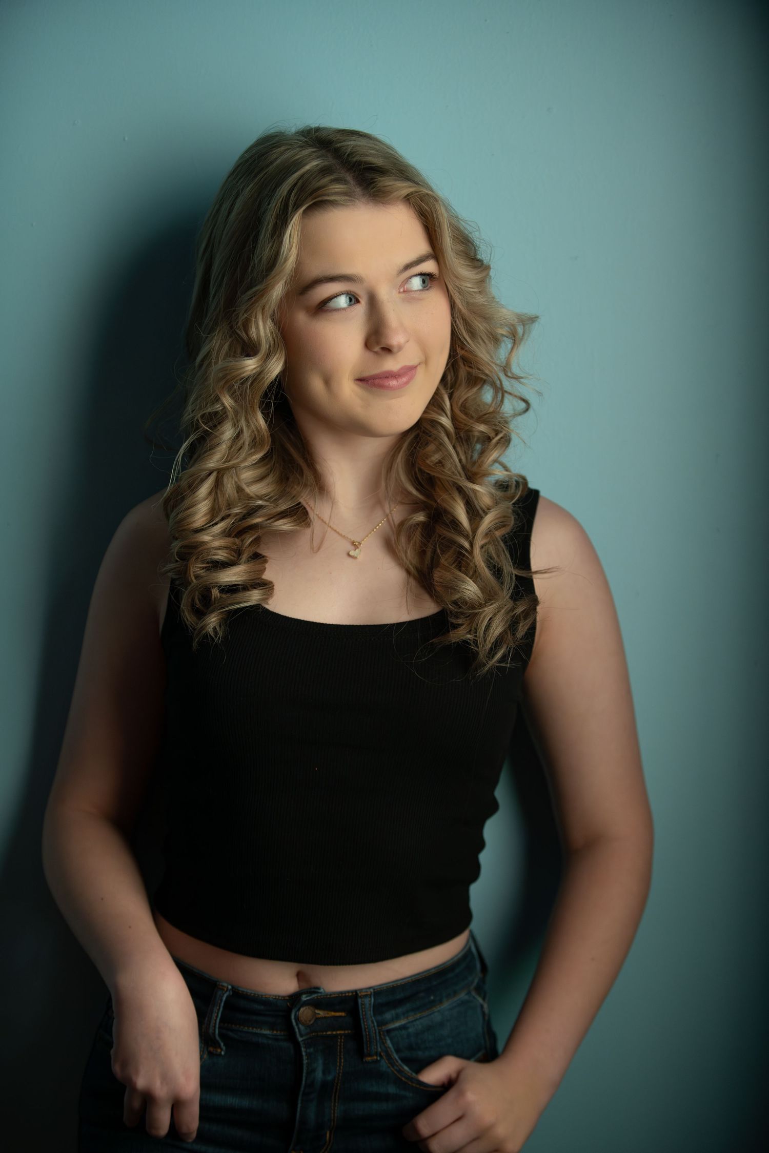 A studio portrait against a teal background featuring casual style and curled hair.