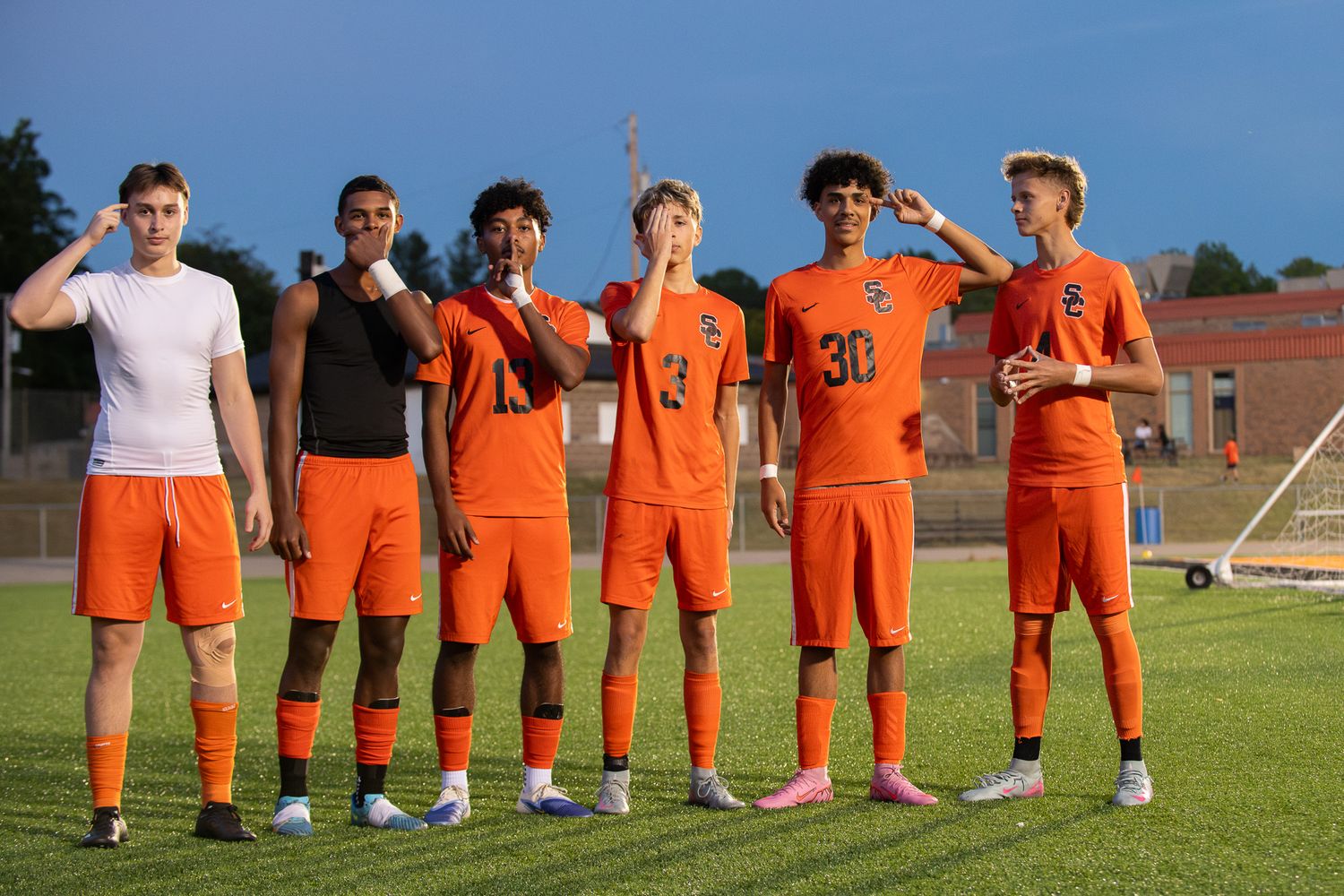 Soccer team in orange uniforms kneeling on grass field during team photo session.