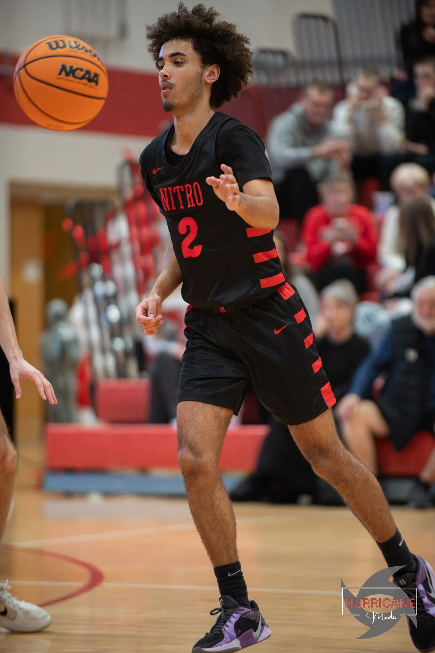 Basketball player in black uniform dribbles the ball during an intense game on indoor court.