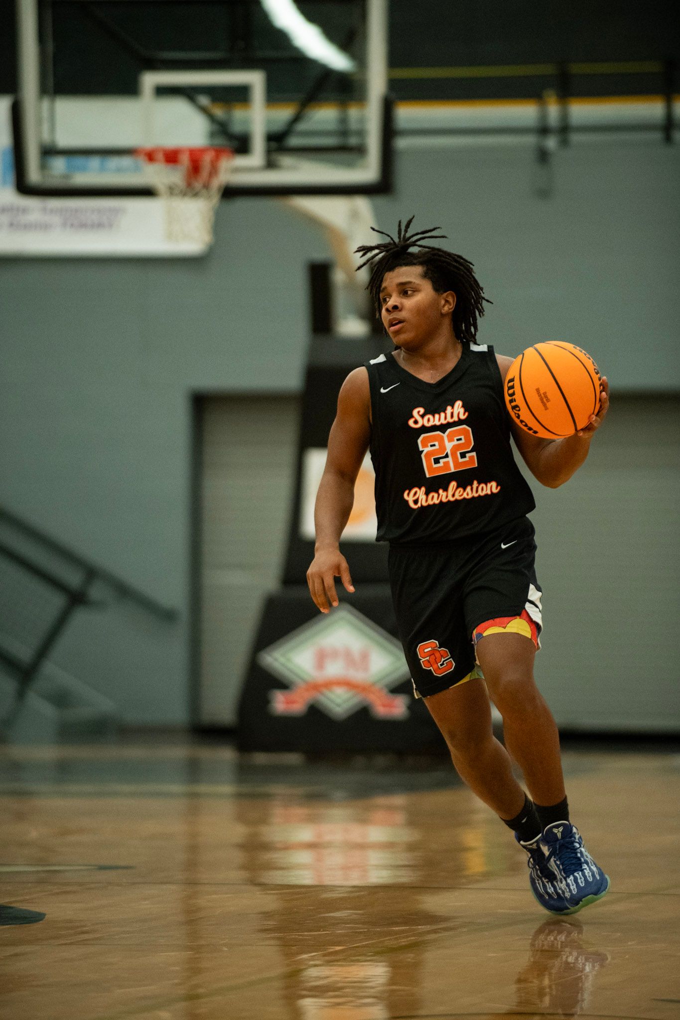 Basketball player in black uniform dribbles across indoor court during practice session.