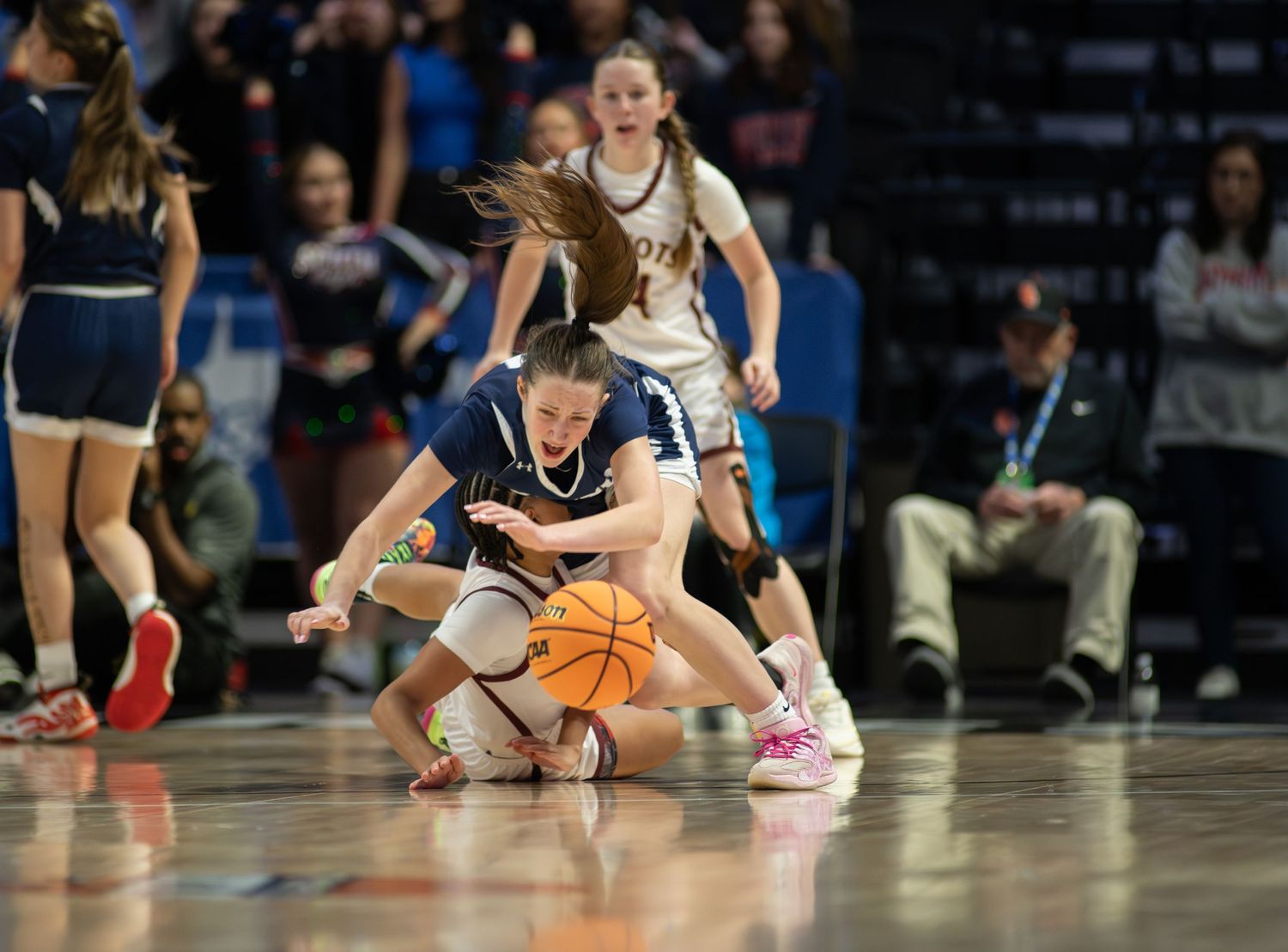 Basketball players dive and scramble for a loose ball during an intense game on the hardwood court.