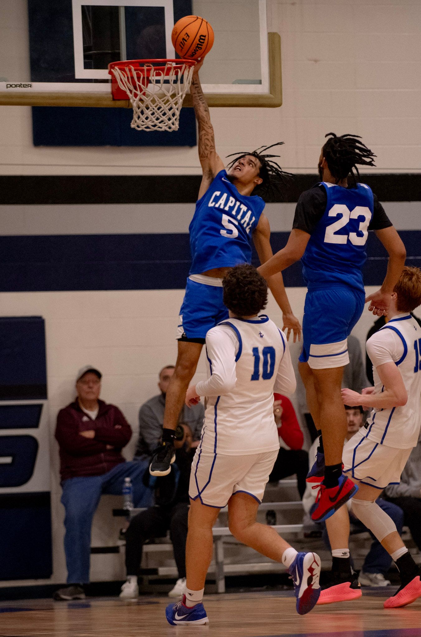 Basketball player in blue uniform soars high above others for a slam dunk at the hoop.