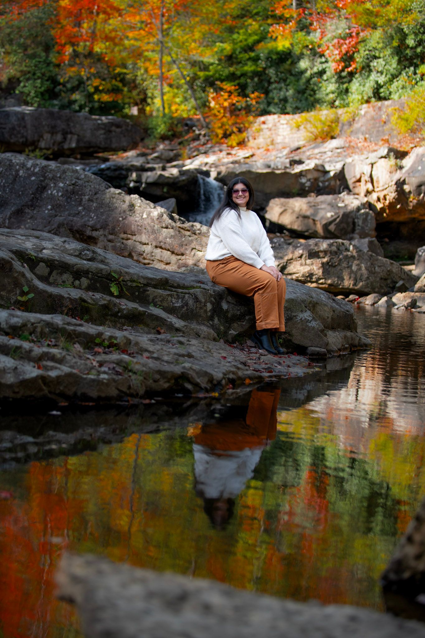 Scenic fall portrait by reflecting pond with vibrant autumn colors in background.