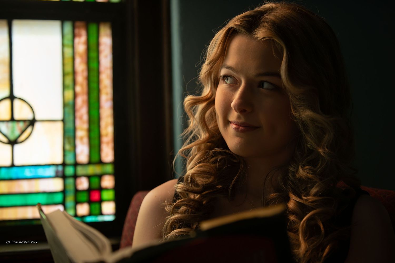 Moody portrait with dramatic lighting against stained glass window background.