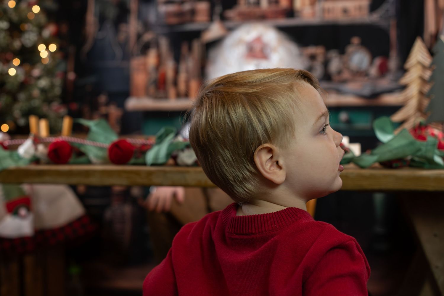 A child looks up at festive holiday decorations in a cozy indoor setting with twinkling lights.