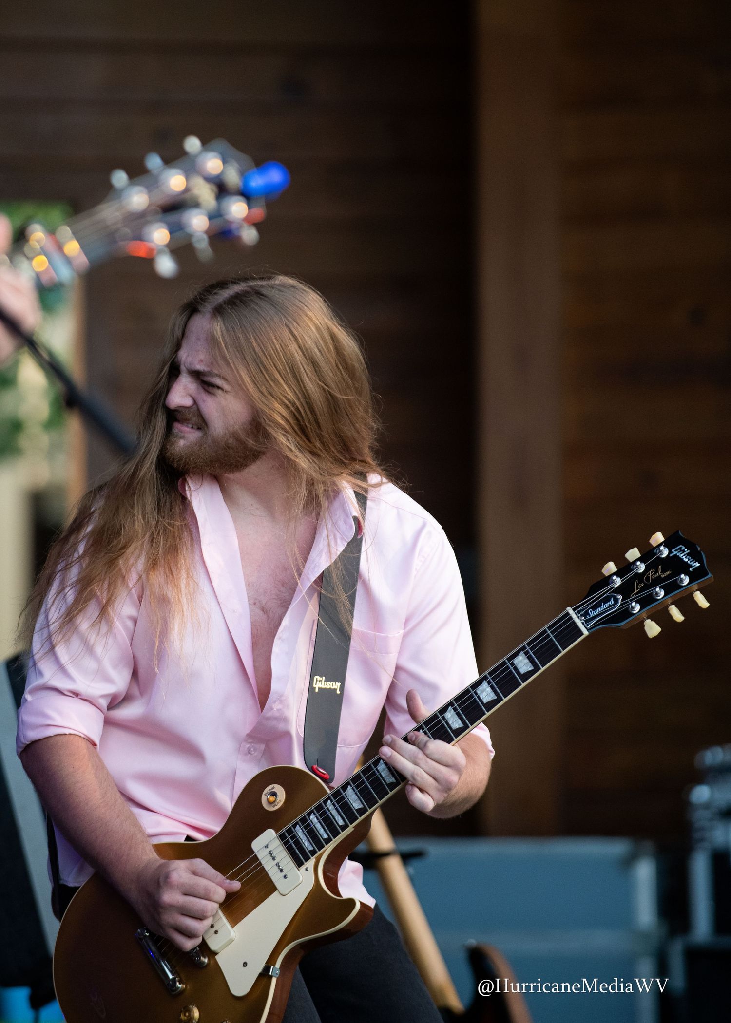 Guitarist in pink shirt performs energetically on gold Les Paul guitar against dark background in progressive sequence.
