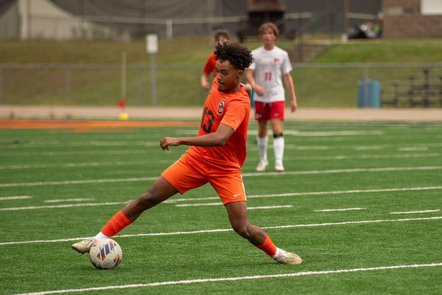 Soccer player in orange uniform dribbles ball on artificial turf field during competitive match.