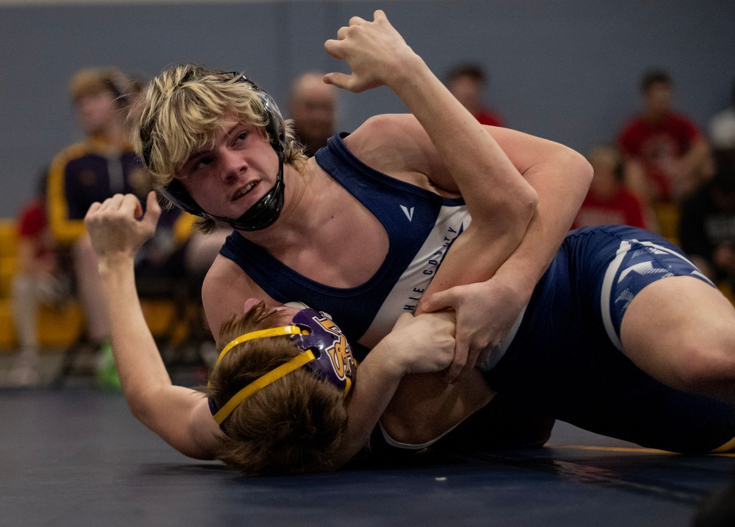 Two wrestlers compete in a high school match on the mat.