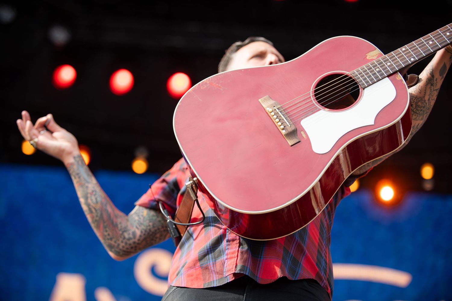 A performer plays a red acoustic guitar on stage with glowing red lights in the background.