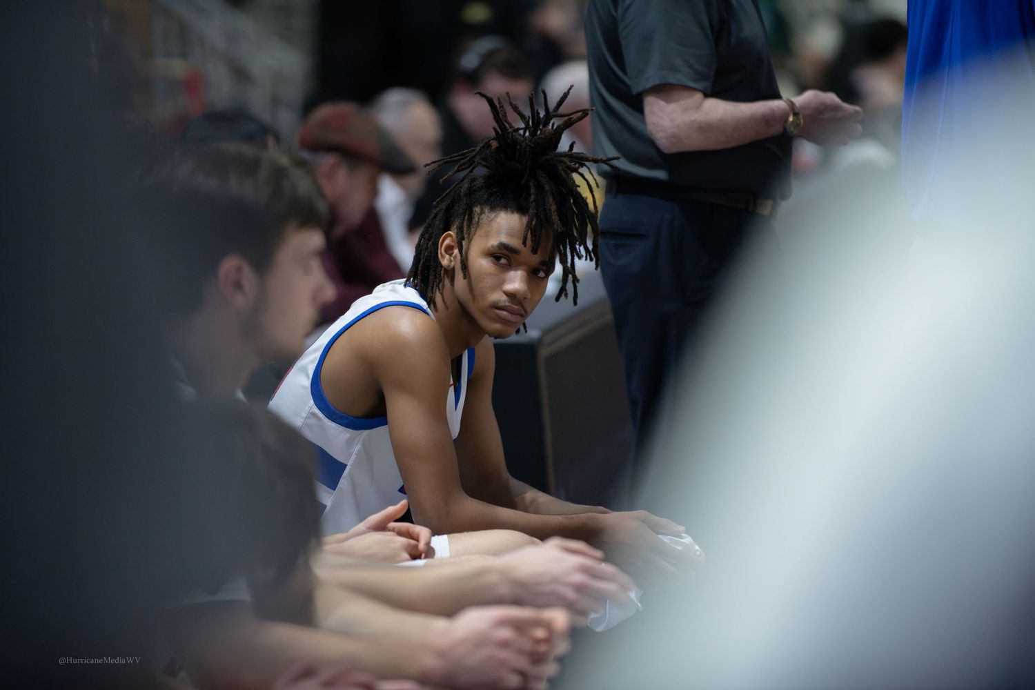 Basketball player sits on sideline bench during game break.
