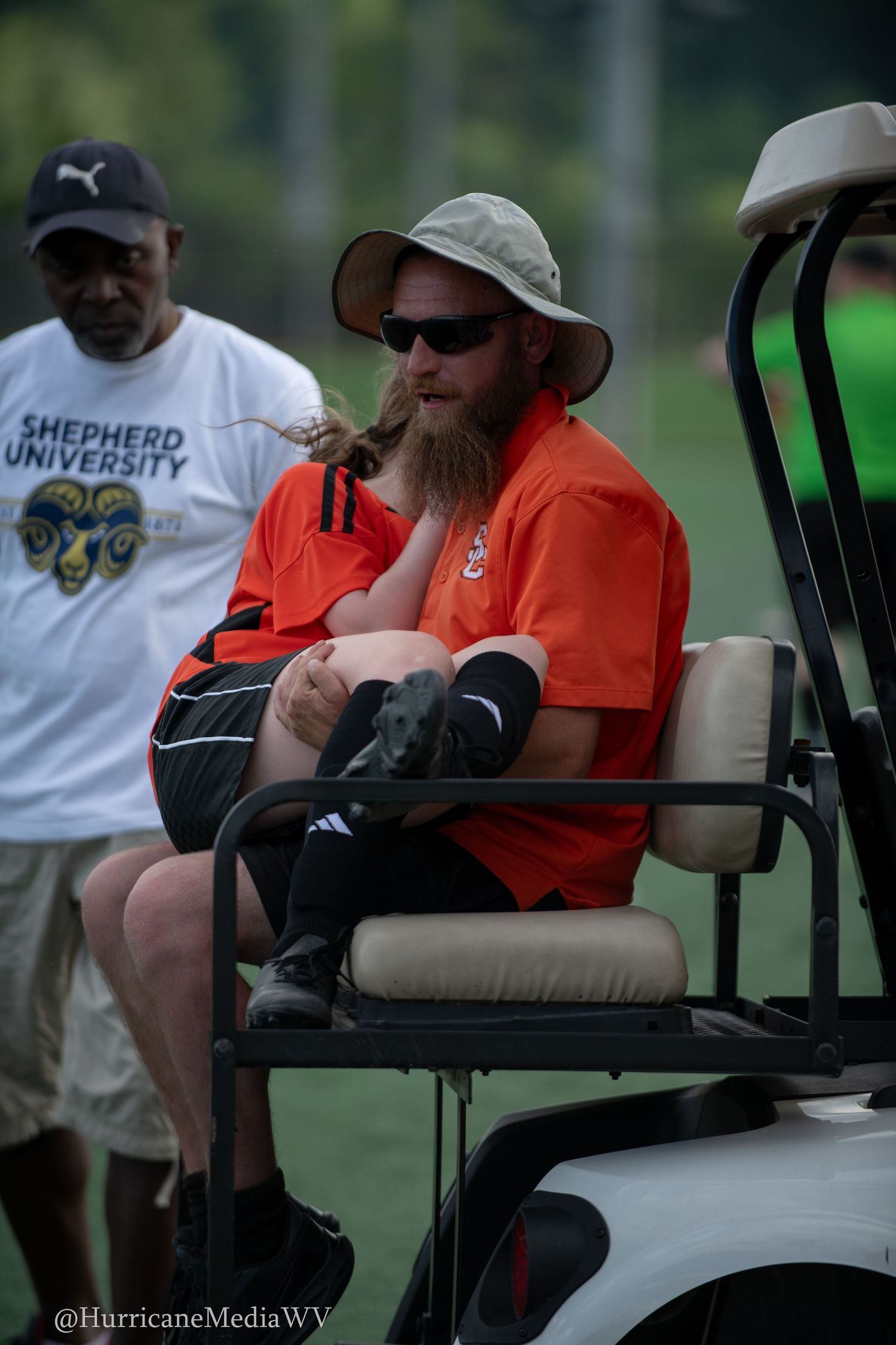 Officials observe sports event from golf cart on sunny day.