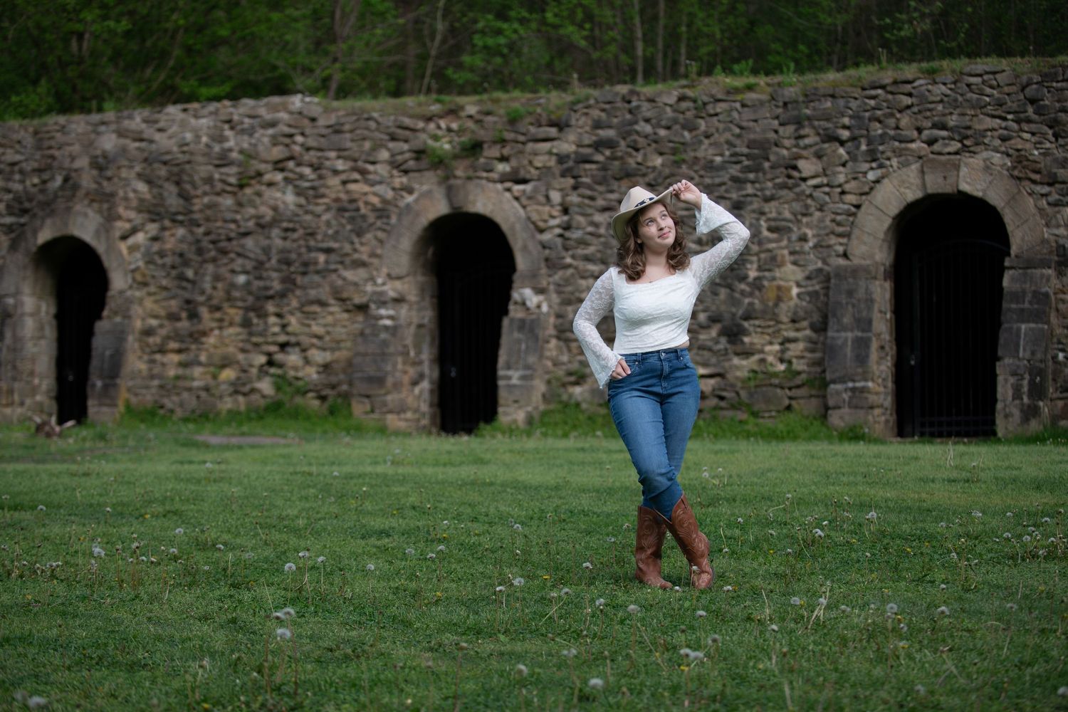 A creative outdoor portrait near stone archways with a casual pose on grassy terrain.