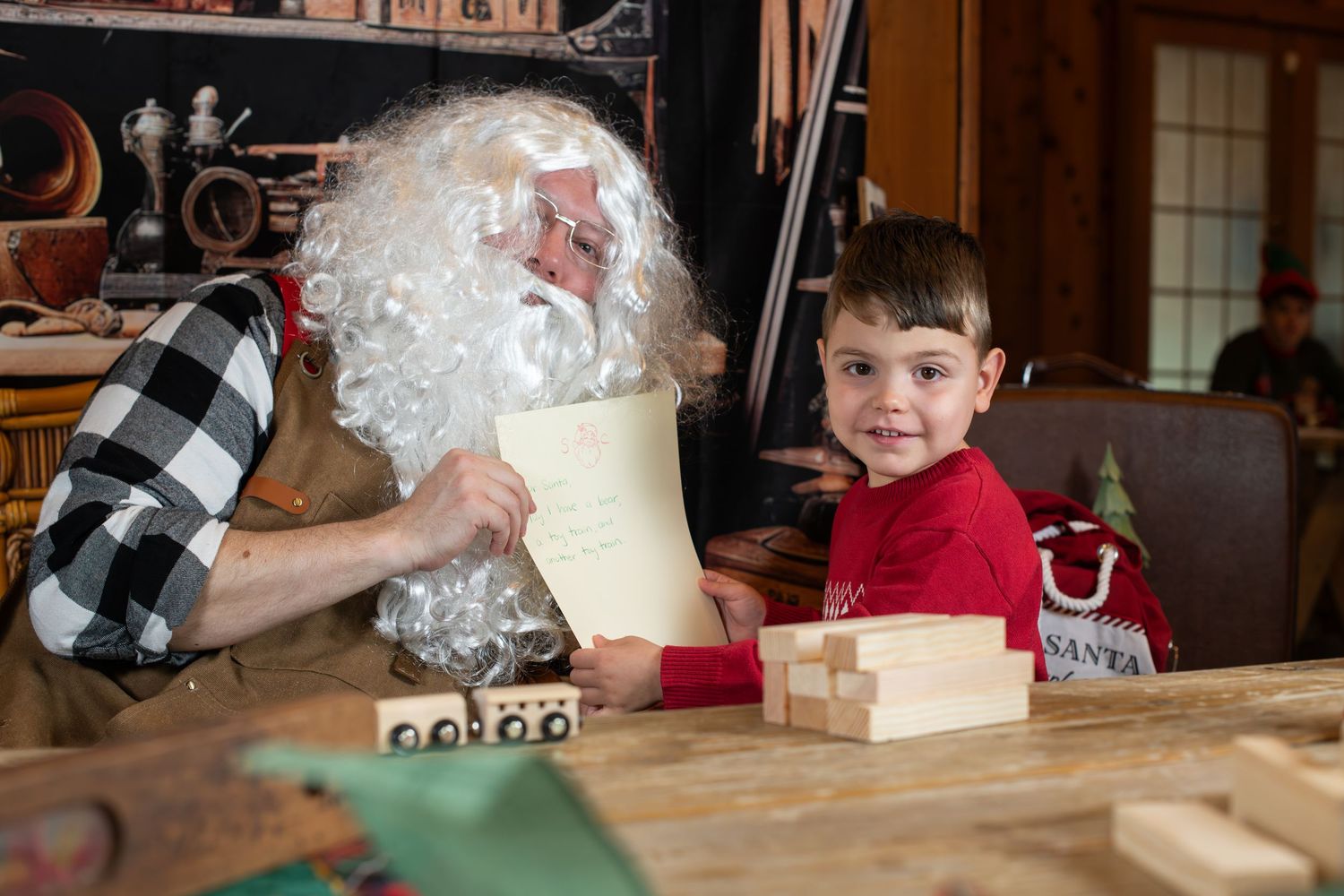 A person in a red sweater works on a woodworking project at a wooden table.