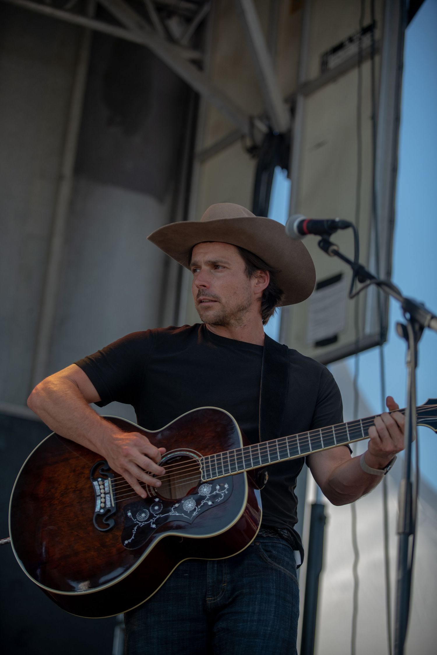 A musician in a cowboy hat plays an acoustic guitar on stage during a performance.