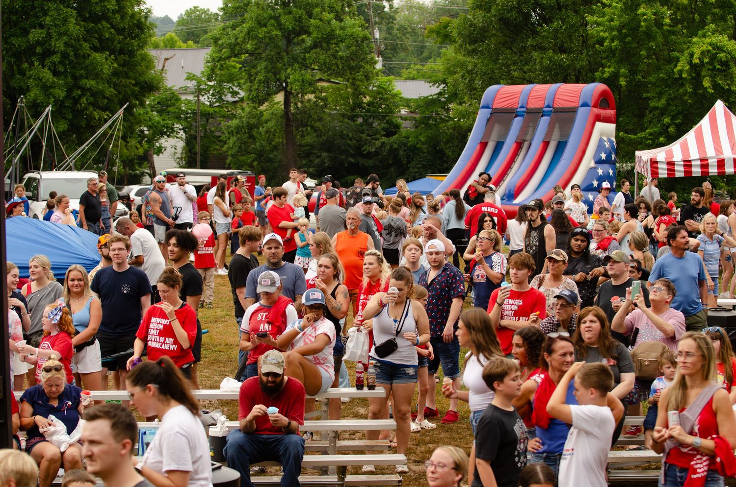 Large crowd gathers at an outdoor summer festival with an inflatable slide in the background.
