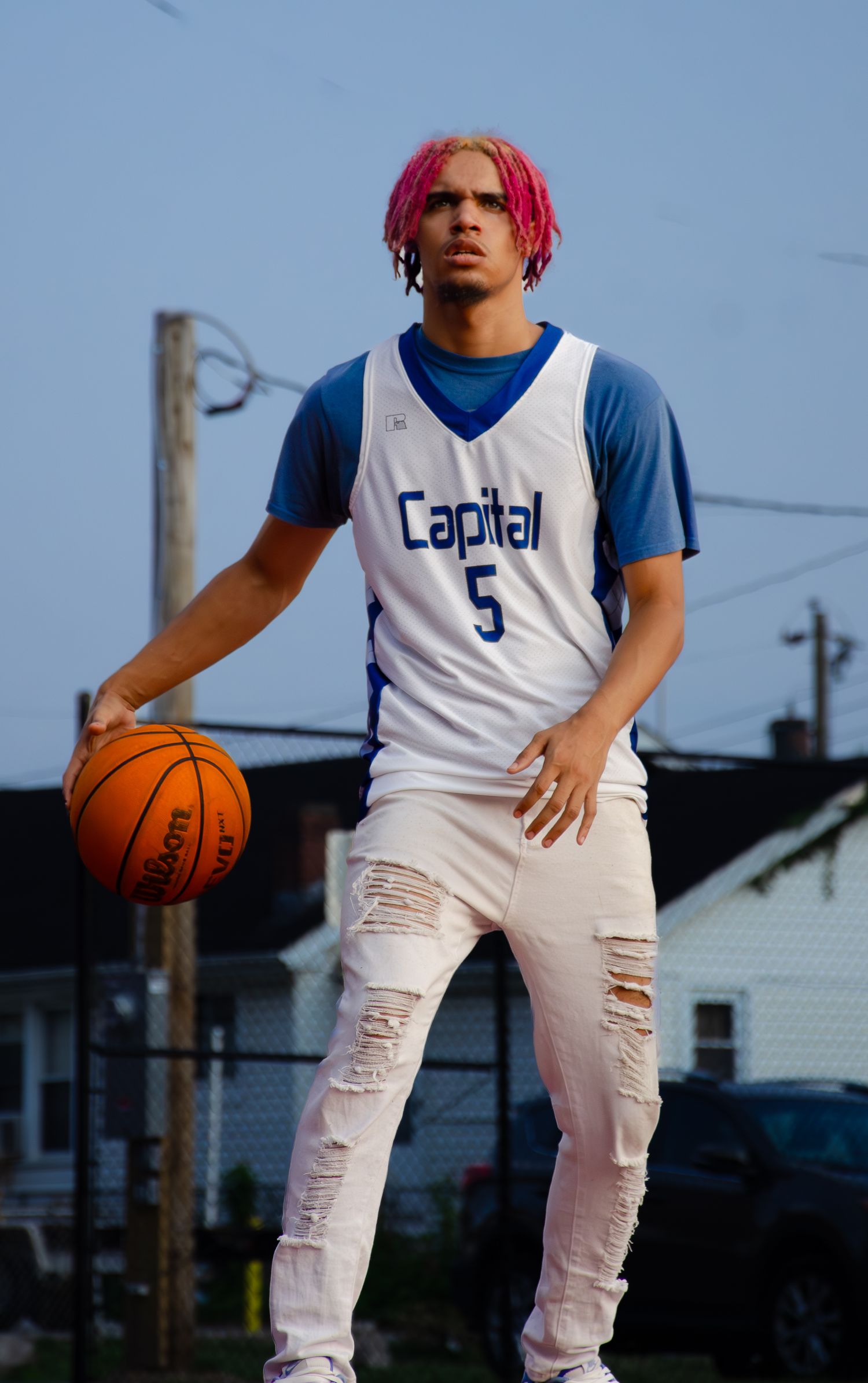 Basketball player in white Capital jersey number 5 posing with ball outdoors.