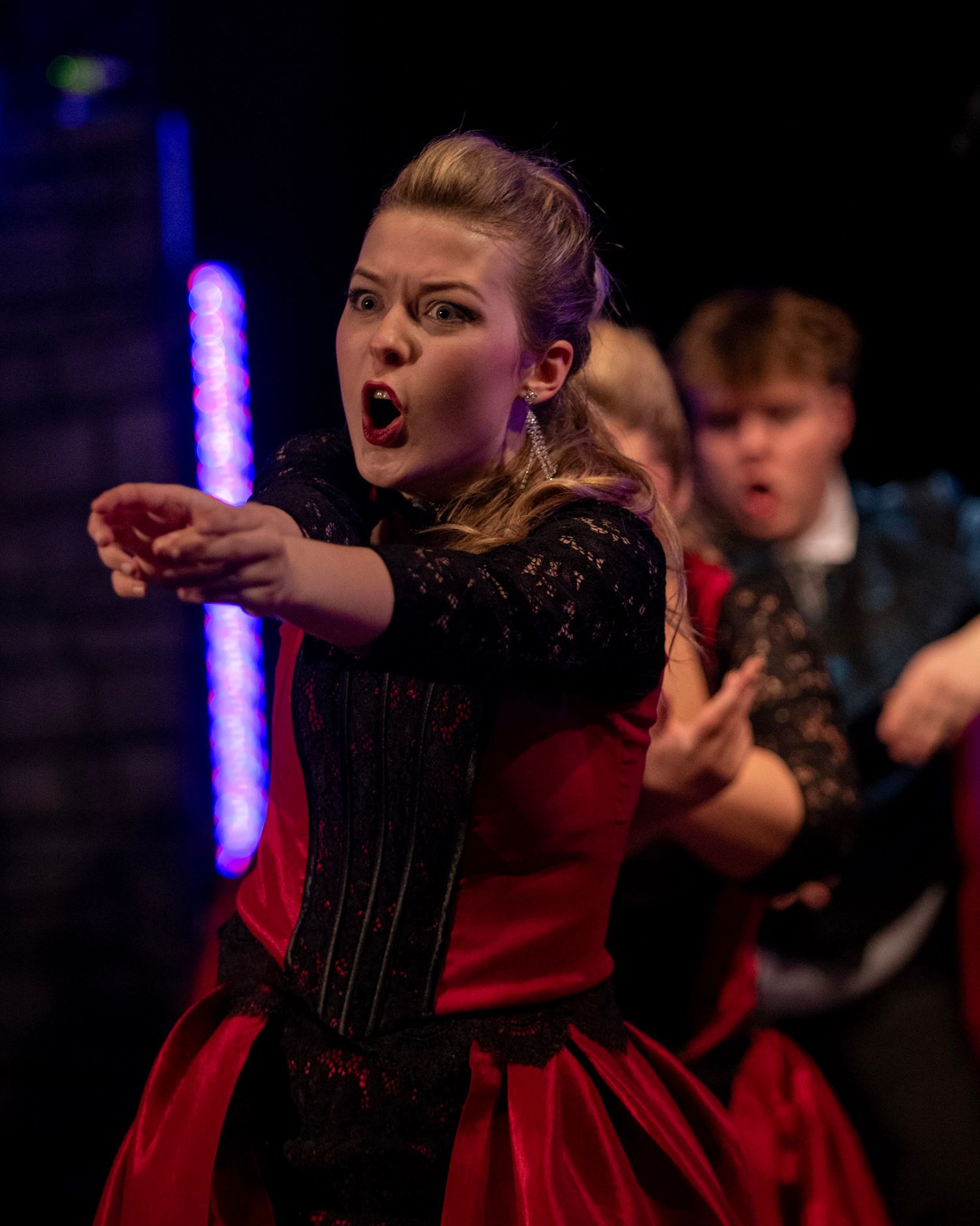 Performer in a red and black costume expressing dramatic emotion during a stage show.