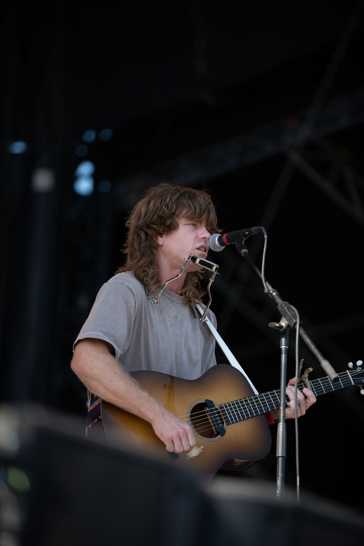 Musician performing on acoustic guitar at a dimly lit concert stage.