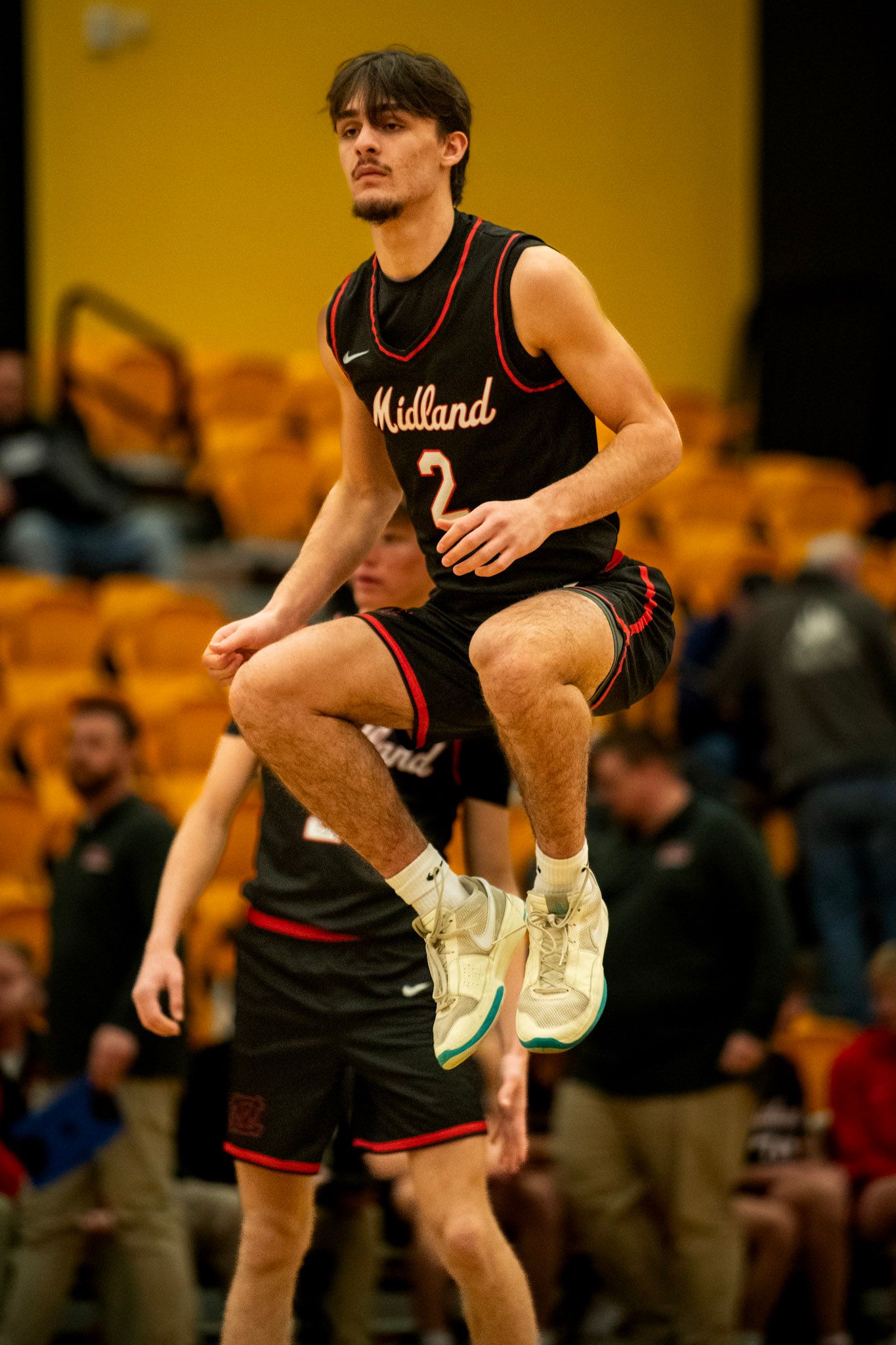 Basketball player in black Midland jersey jumps during indoor game with yellow background.