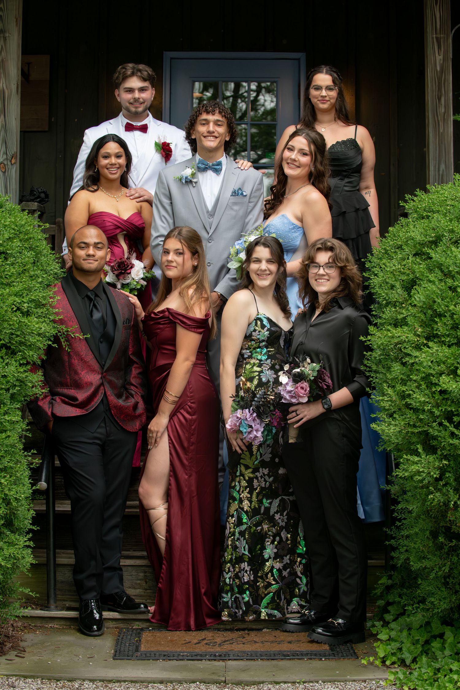 A formal group photo showing people dressed in burgundy and black attire standing on porch steps.